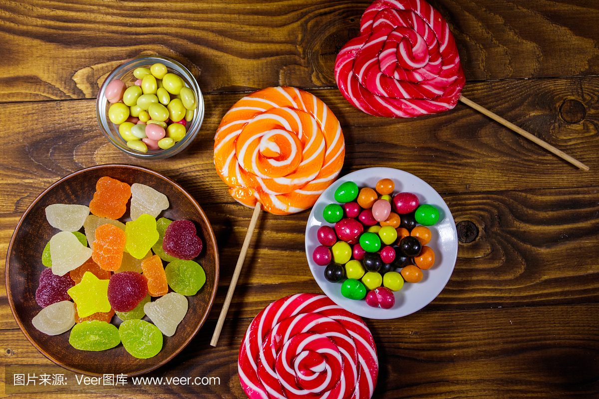 木桌上放着五颜六色的巧克力糖果、棒棒糖和果冻糖果