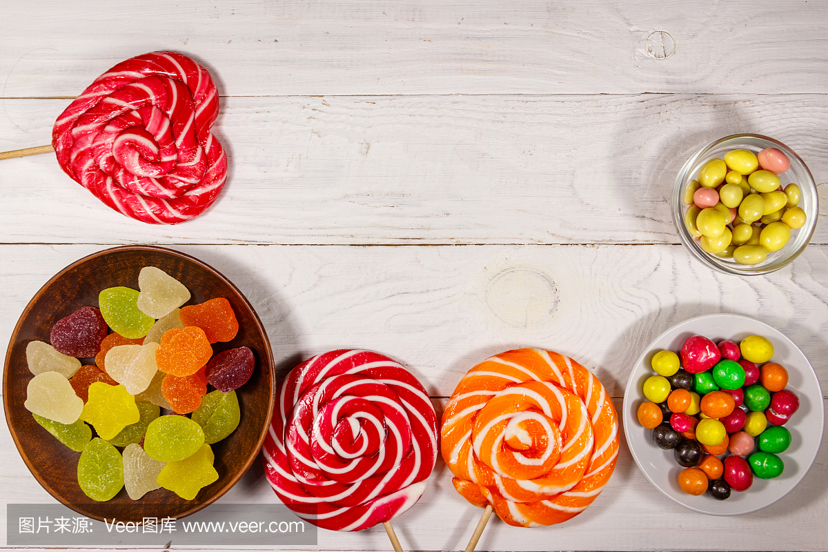 白色的木桌上放着五颜六色的巧克力糖果、棒棒糖和果冻糖果